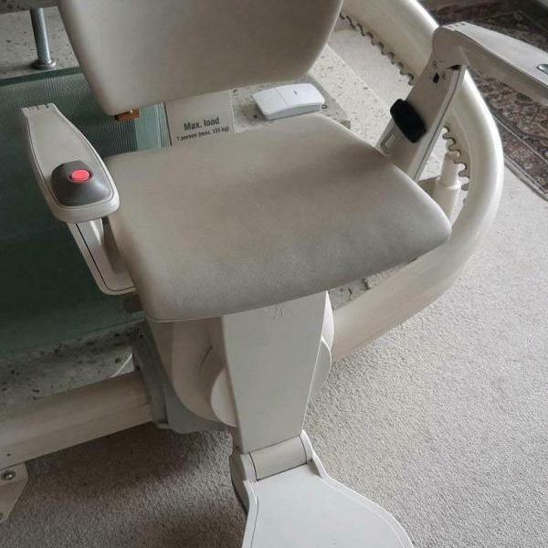 Ein grauer Badestuhl mit Armlehnen und Sitzfläche auf einem Rollstuhl.